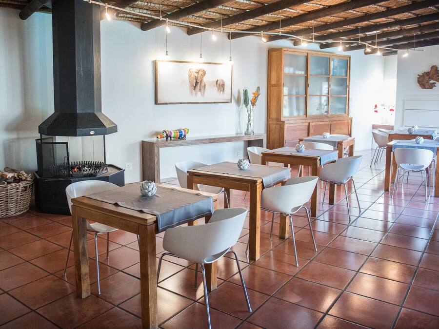 A rustic dining area with wooden tables and white chairs, a large black chimney, and a wooden cabinet with glass doors.