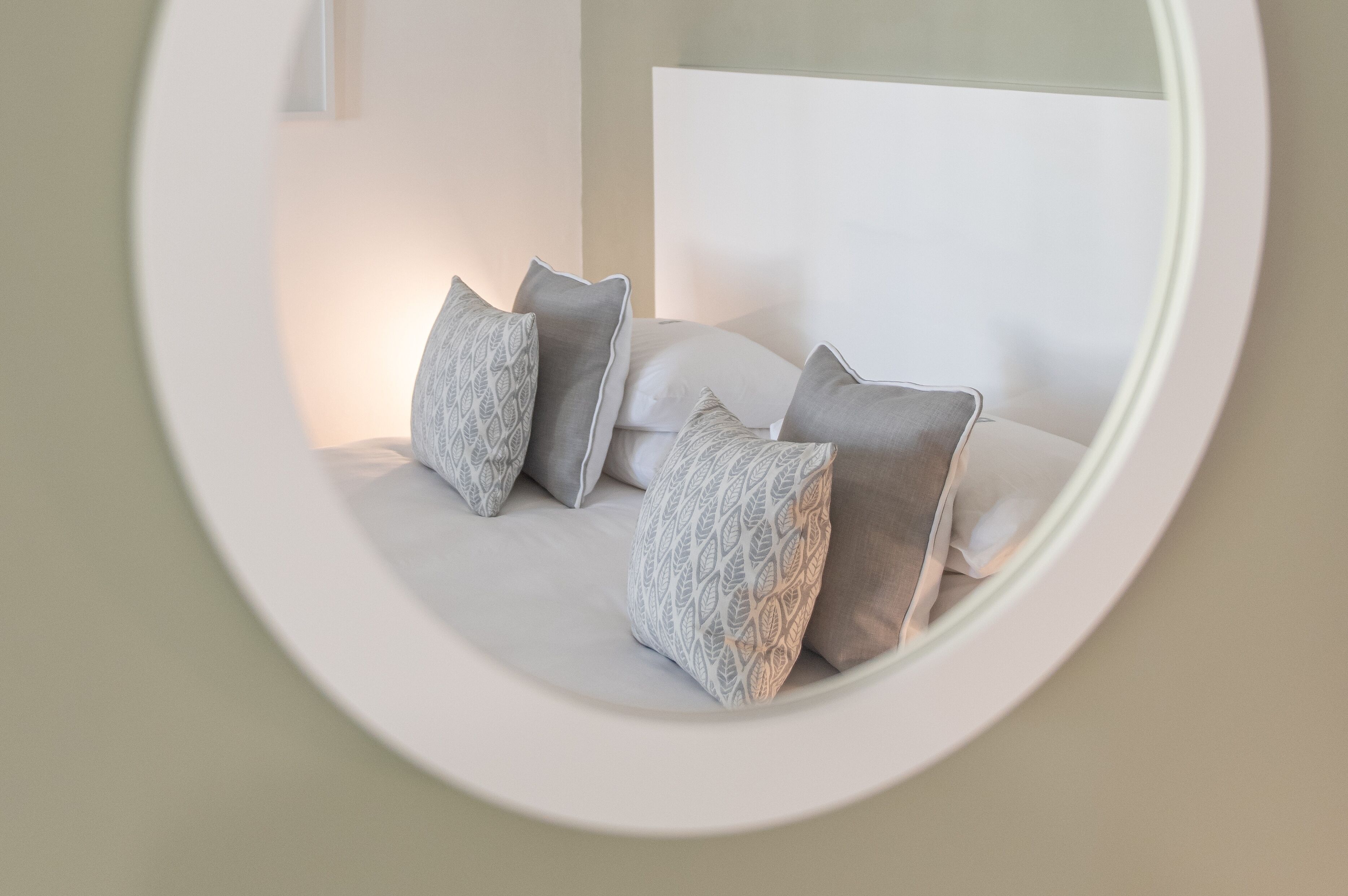 A circular mirror reflecting a bed with a white headboard and patterned pillows.