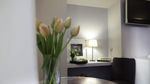 Un salon moderne avec une table en verre, un canapé foncé, une lampe et un téléviseur fixé au mur.