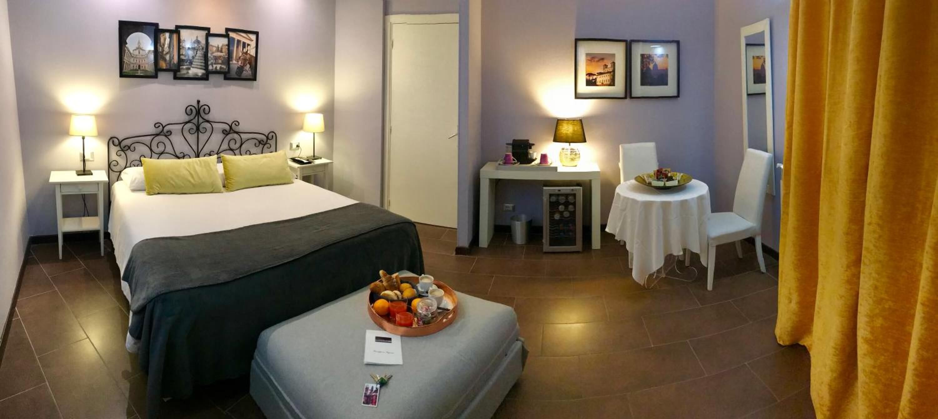 Una camera d'albergo con un letto, comodini, un tavolino con una lampada, una sedia e un vassoio con prodotti per la colazione.