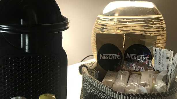 Une machine à café, un panier de capsules Nescafé et un présentoir à dosettes de café Nescafé sur une table.