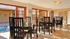 A dining area with a pool view, wooden chairs, a table with a vase, and a clock on the wall. - Apple Tree Guest House (Stellenbosch)