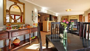 A dining area with a large mirror, wooden furniture, and a vase with flowers. - Apple Tree Guest House (Stellenbosch)
