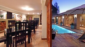 An indoor pool area with a dining area, wooden chairs, and a stone wall. - Apple Tree Guest House (Stellenbosch)