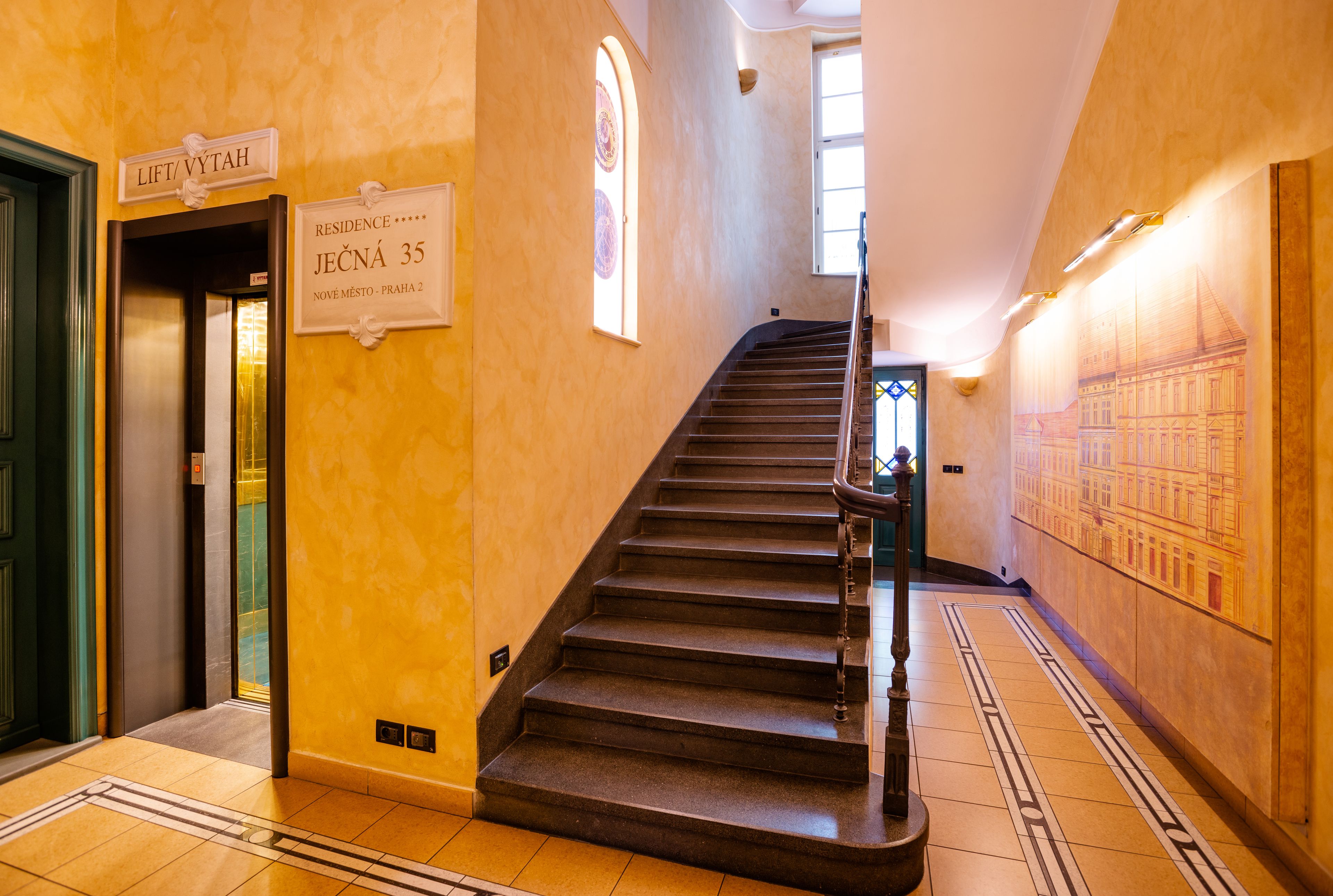 Un escalier dans le hall d’un hôtel, avec des panneaux indiquant les numéros de chambre et un ascenseur.