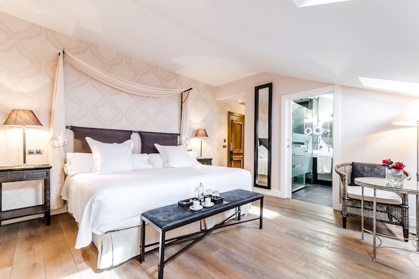 A hotel room with a large bed, bedside tables, a glass coffee table, and a view of the bathroom.