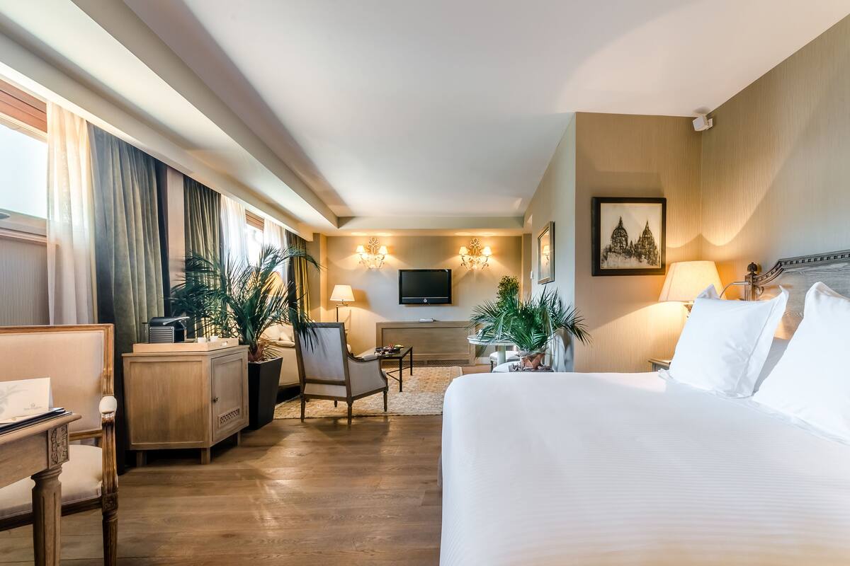 Ein Hotelzimmer mit einem großen Bett, einem Schreibtisch, einem Sessel, einem Fernseher und zwei Wandlampen.