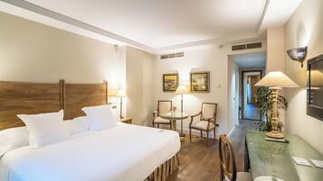 Una habitación de hotel con una cama grande, una mesita con sillas, una lámpara y cuadros en la pared.