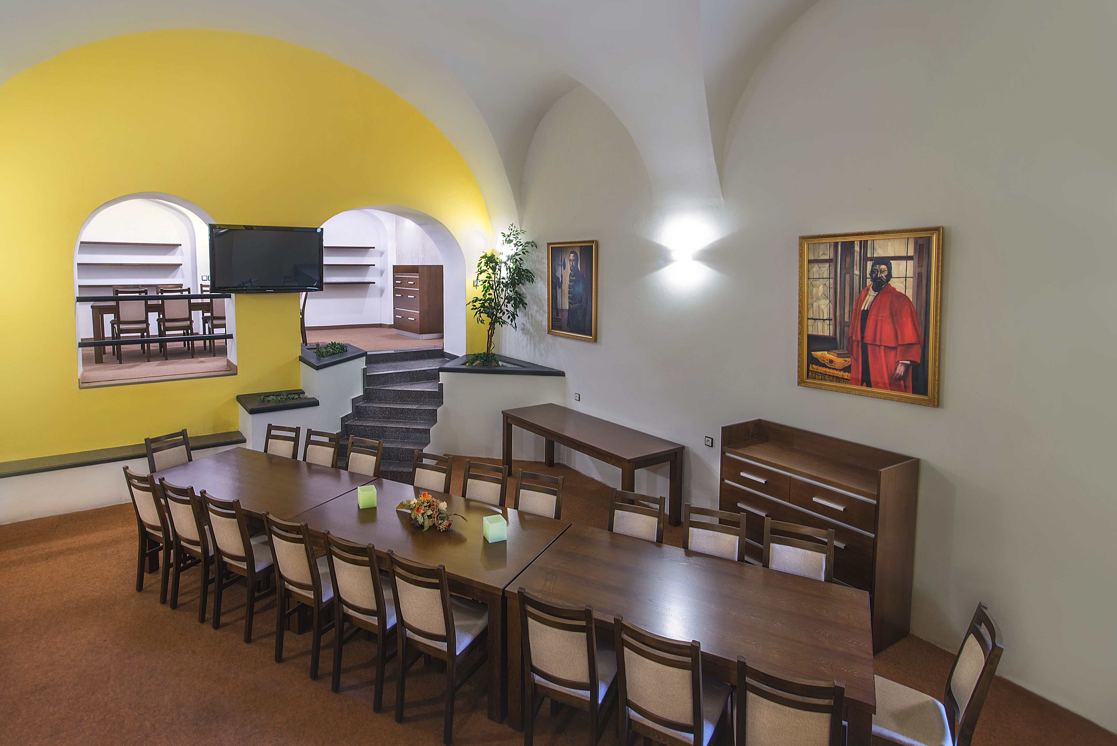 A dining area with a long wooden table and chairs, a staircase, and a yellow wall.