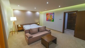 A modern hotel room with a bed, a sofa, a coffee table, a painting, and a wooden door.