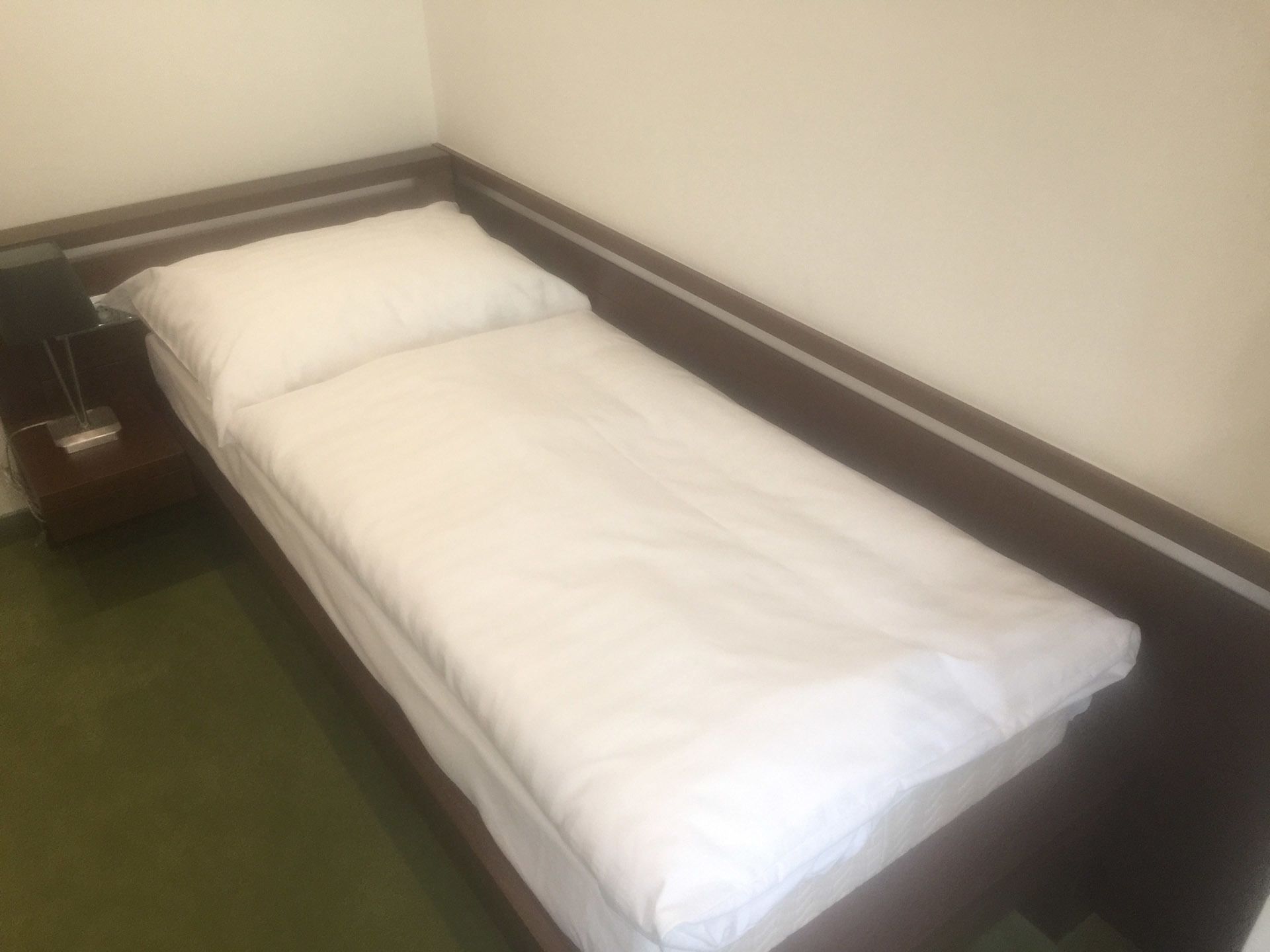 A single bed with white bedding in a room with a green carpet and a wooden headboard.