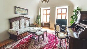 A living room with a sofa, coffee table, and a piano. There is a large window and a chandelier.