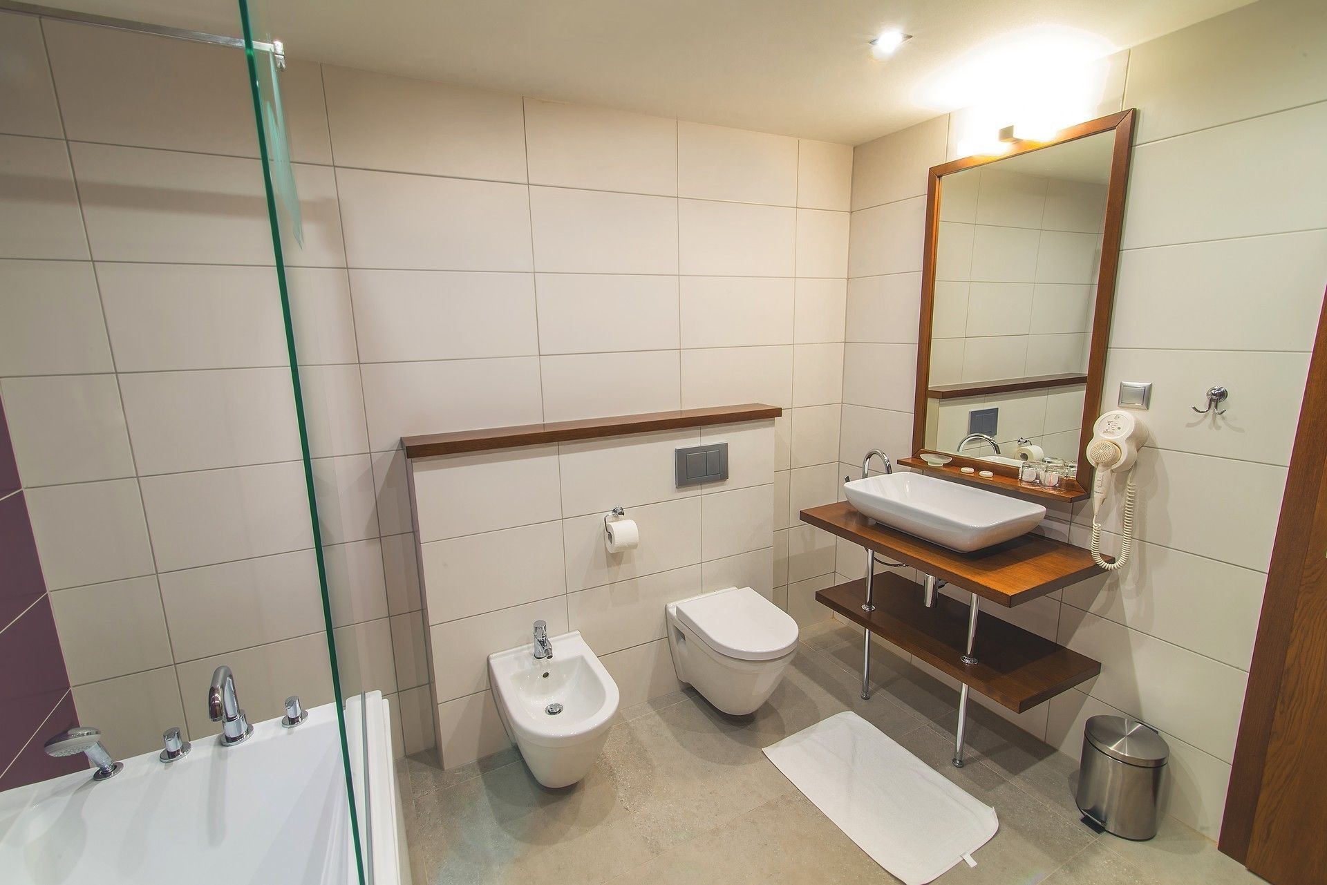 A modern bathroom with a glass shower enclosure, a bidet, a toilet, a sink with a mirror, and a hairdryer.