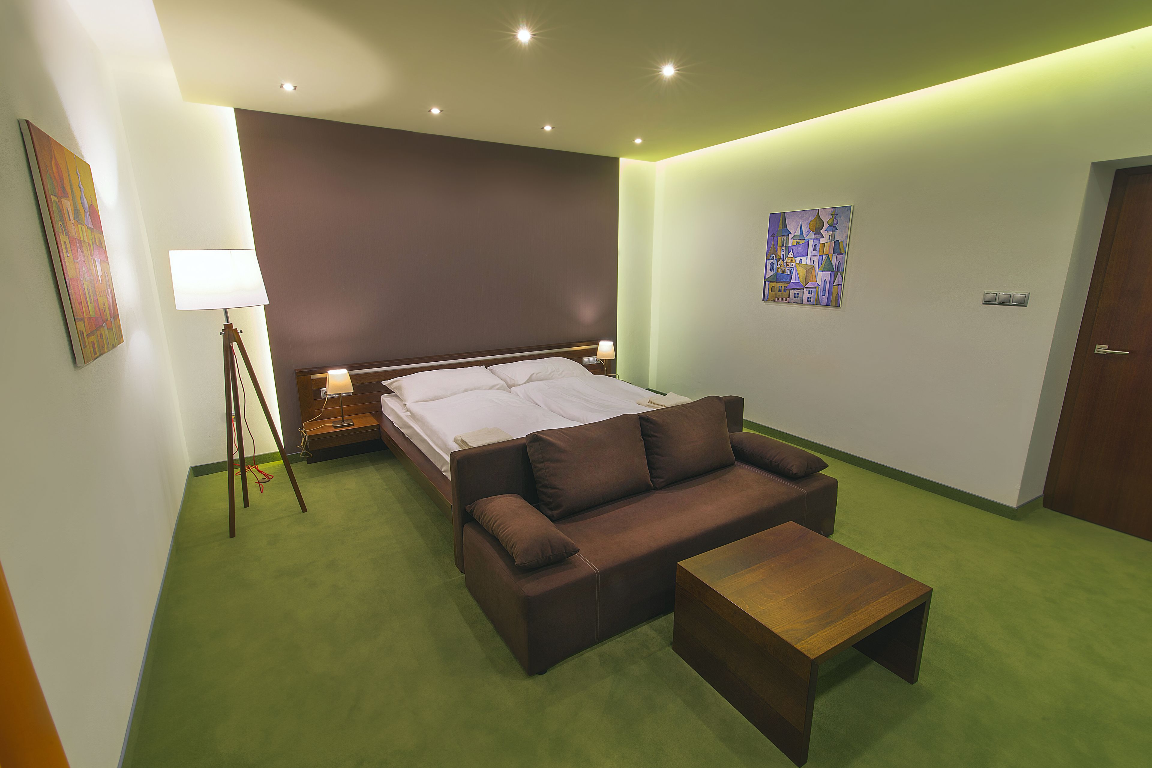 Una habitación de hotel moderna con una cama, un sofá, una mesa de centro de madera y una lámpara de pie.