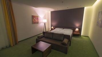 A hotel room with a bed, a sofa, a small table, and a floor lamp.