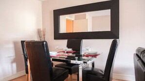 Un comedor con una mesa dispuesta para cuatro personas, sillas negras y un espejo grande sobre la mesa.
