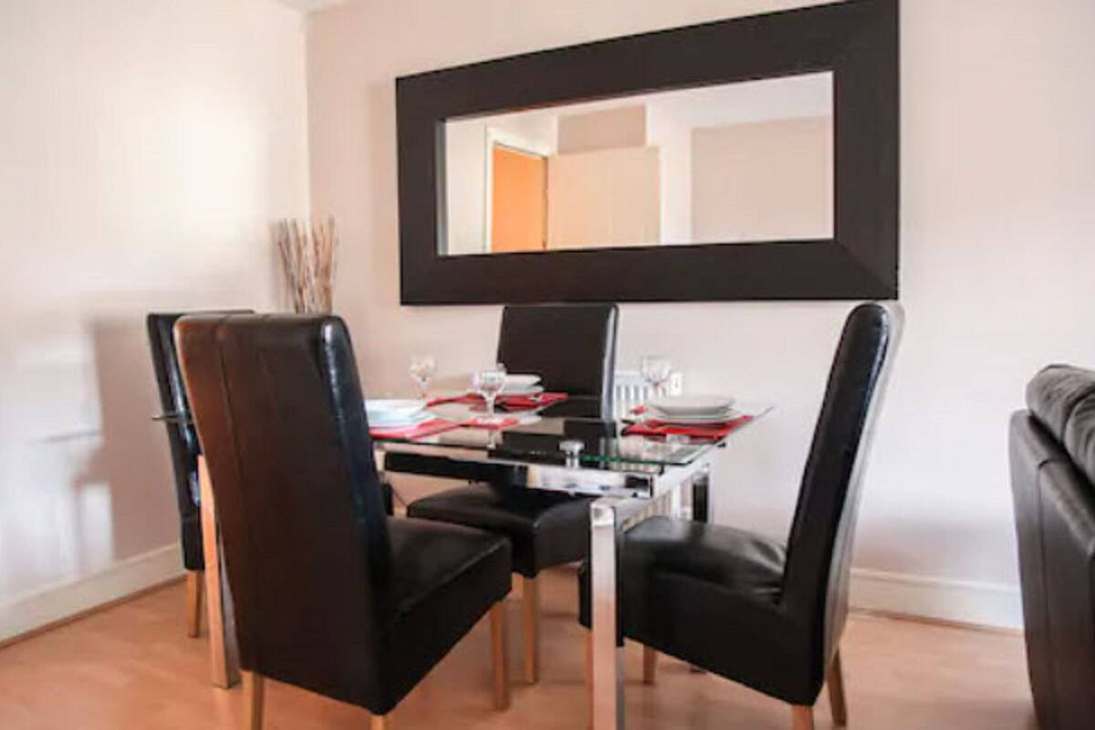 A dining area with a table set for four, black chairs, and a large mirror above the table.