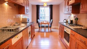 Una cocina con armarios de madera, una mesa de comedor con sillas, un fregadero, una estufa y una ventana con cortinas.