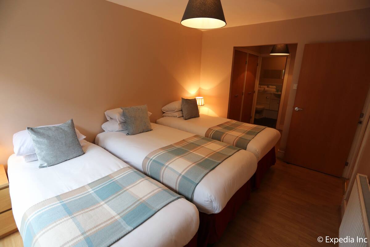 A hotel room with three beds, each with a plaid blanket and pillows. There is a wooden door and a radiator on the wall.