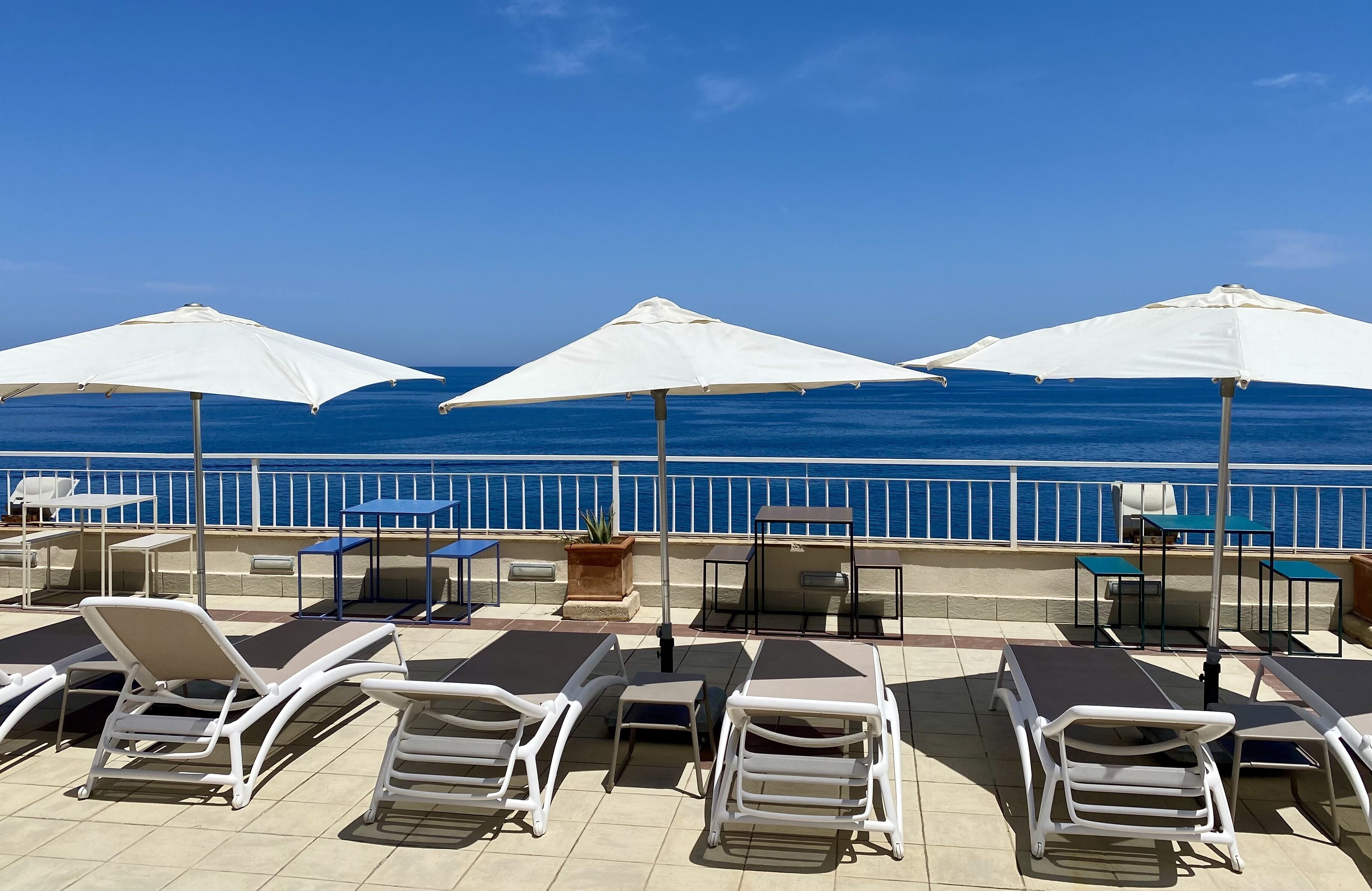 Een zonnig buitenzitgedeelte met lounge stoelen en parasols, met uitzicht op een rustige zee.