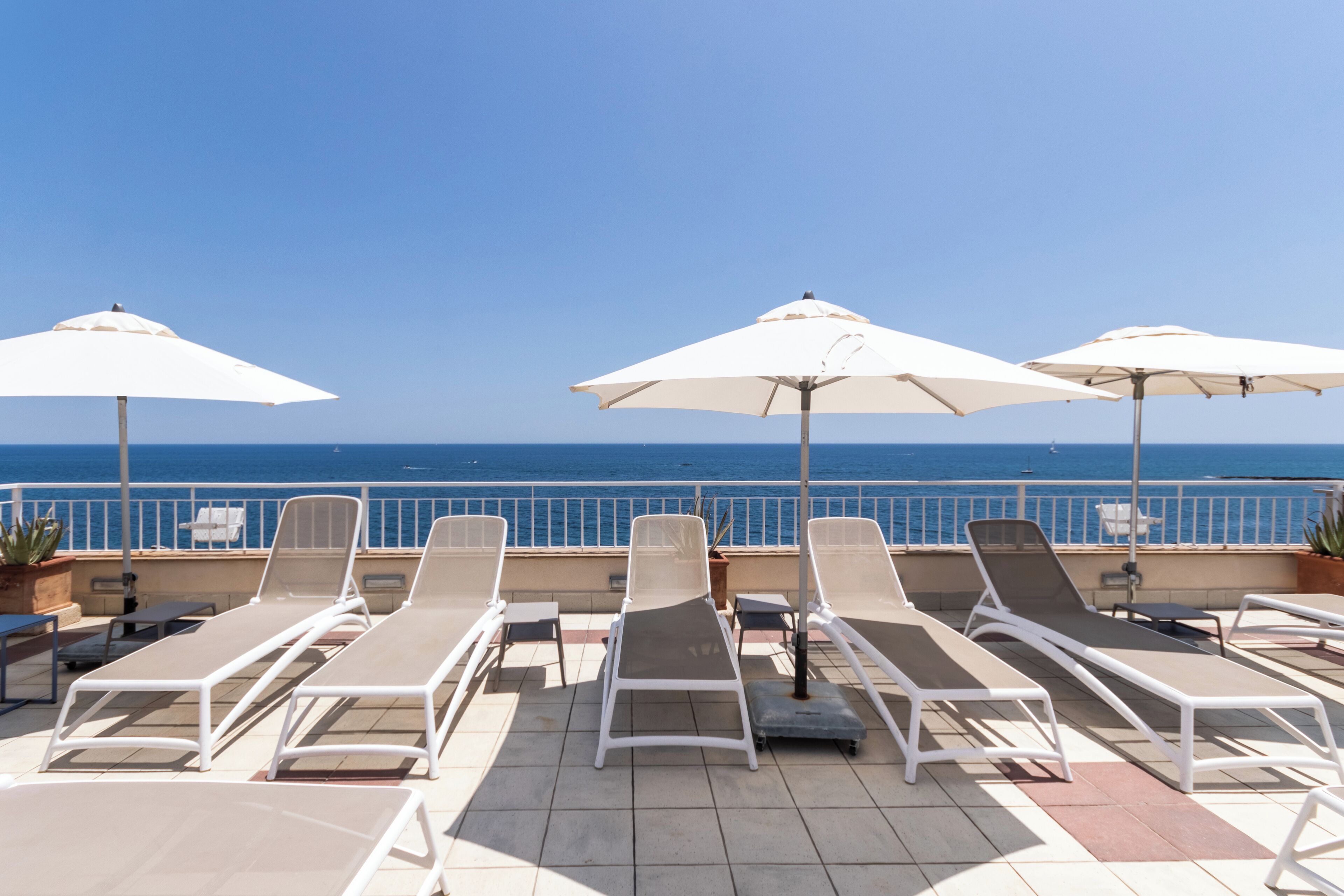 Een terras op het dak met ligbedden en parasols, met uitzicht op zee.