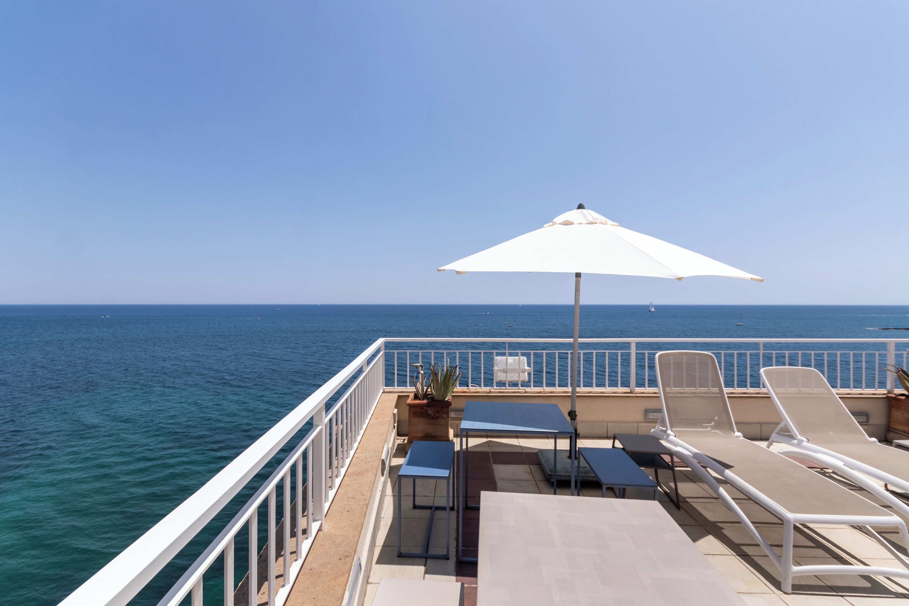 A deck with lounge chairs, a table, and an umbrella overlooking the sea.