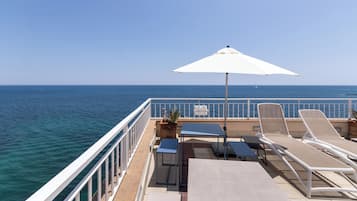 A deck with lounge chairs, a table, and an umbrella overlooking the sea.