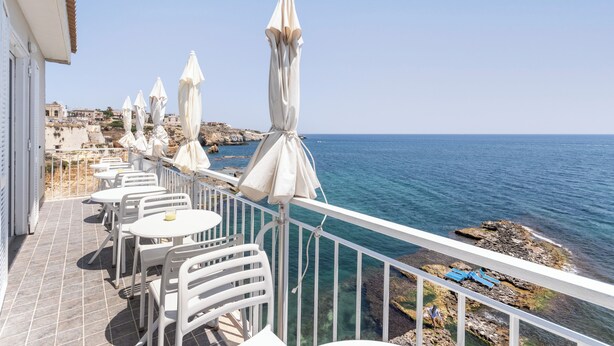 Een terras met witte tafels en stoelen, witte parasols en uitzicht op zee.