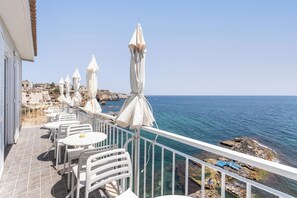 A terrace with white tables and chairs, white umbrellas, and a view of the sea.