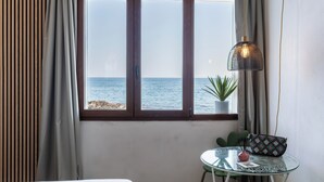 Een kamer met een groot raam met uitzicht op zee, een kleine tafel met een plantje en een hanglamp.