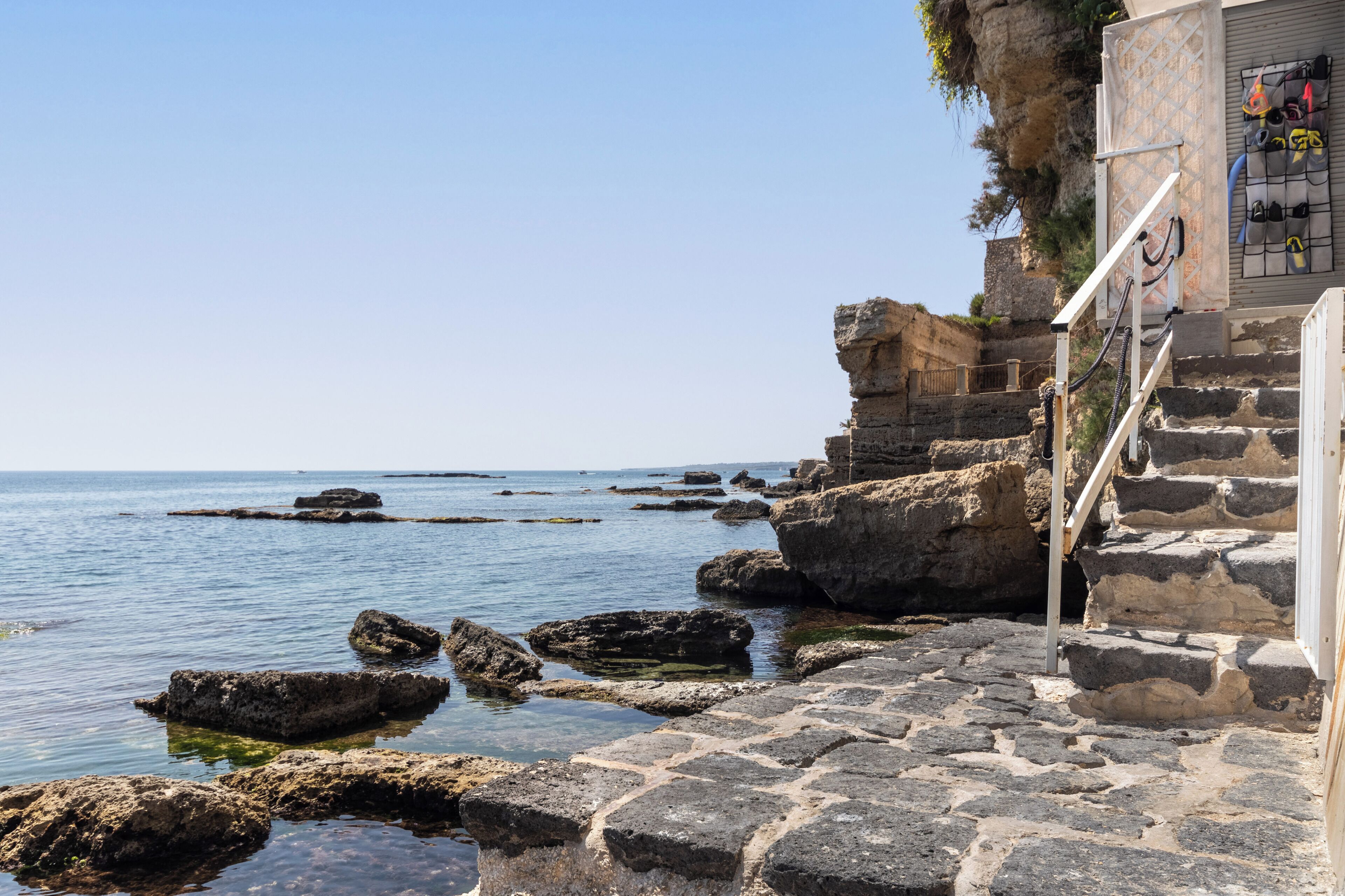 Una escalera de piedra desciende hacia una costa rocosa con agua azul cristalina.