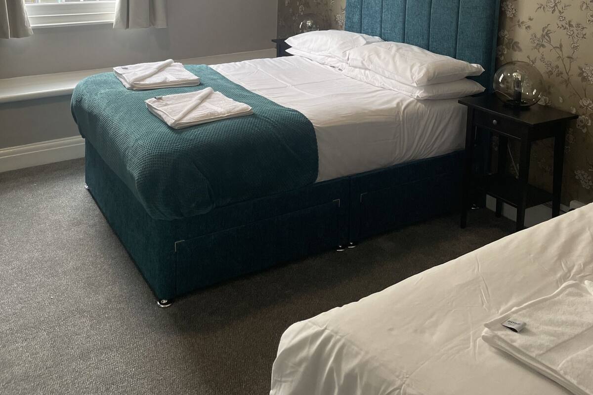 Quarto com uma cama, uma janela, uma mesa de cabeceira e uma parede com papel de parede floral.