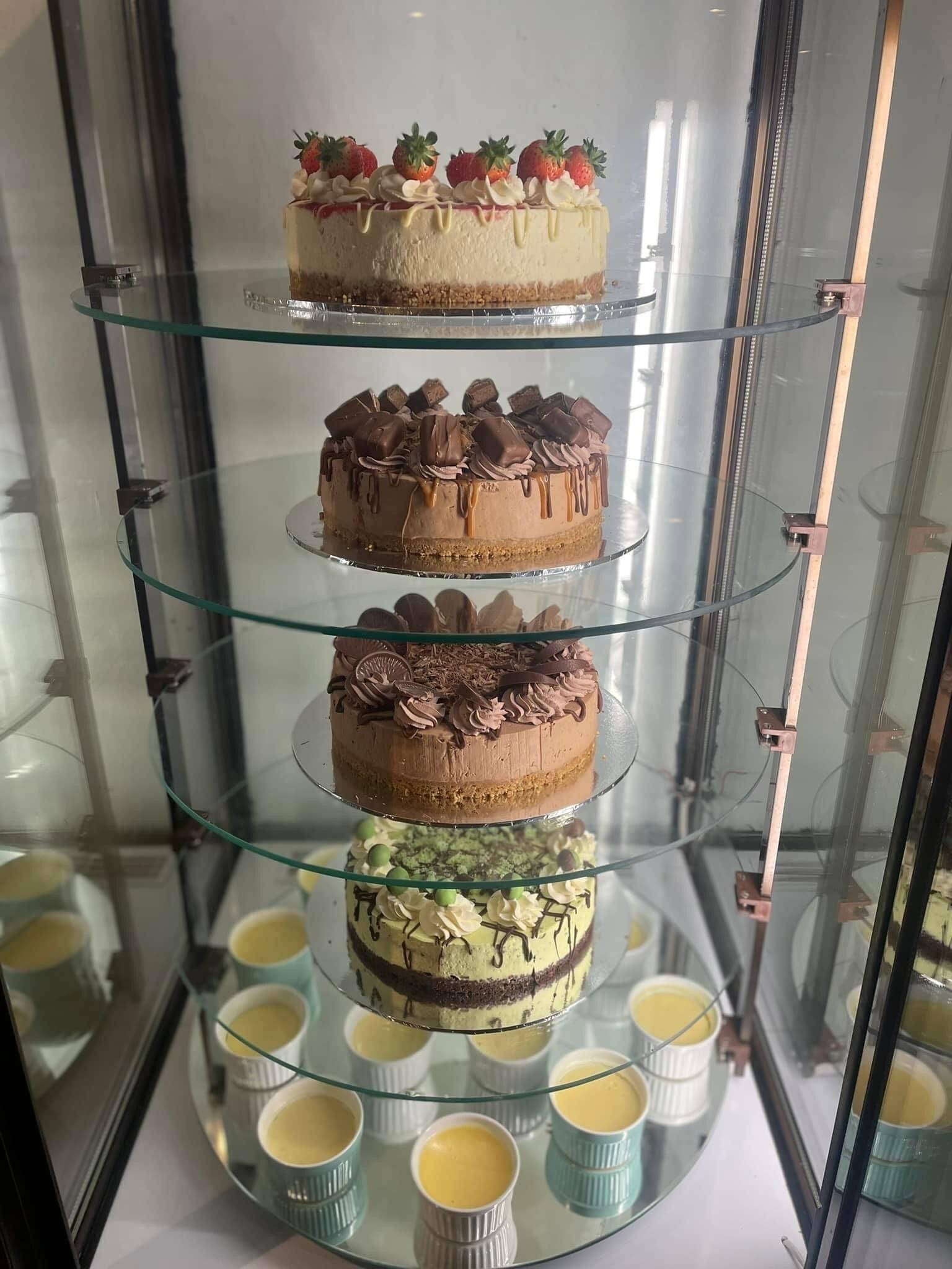 Un expositor escalonado con varios pasteles y pequeños vasos de postres.