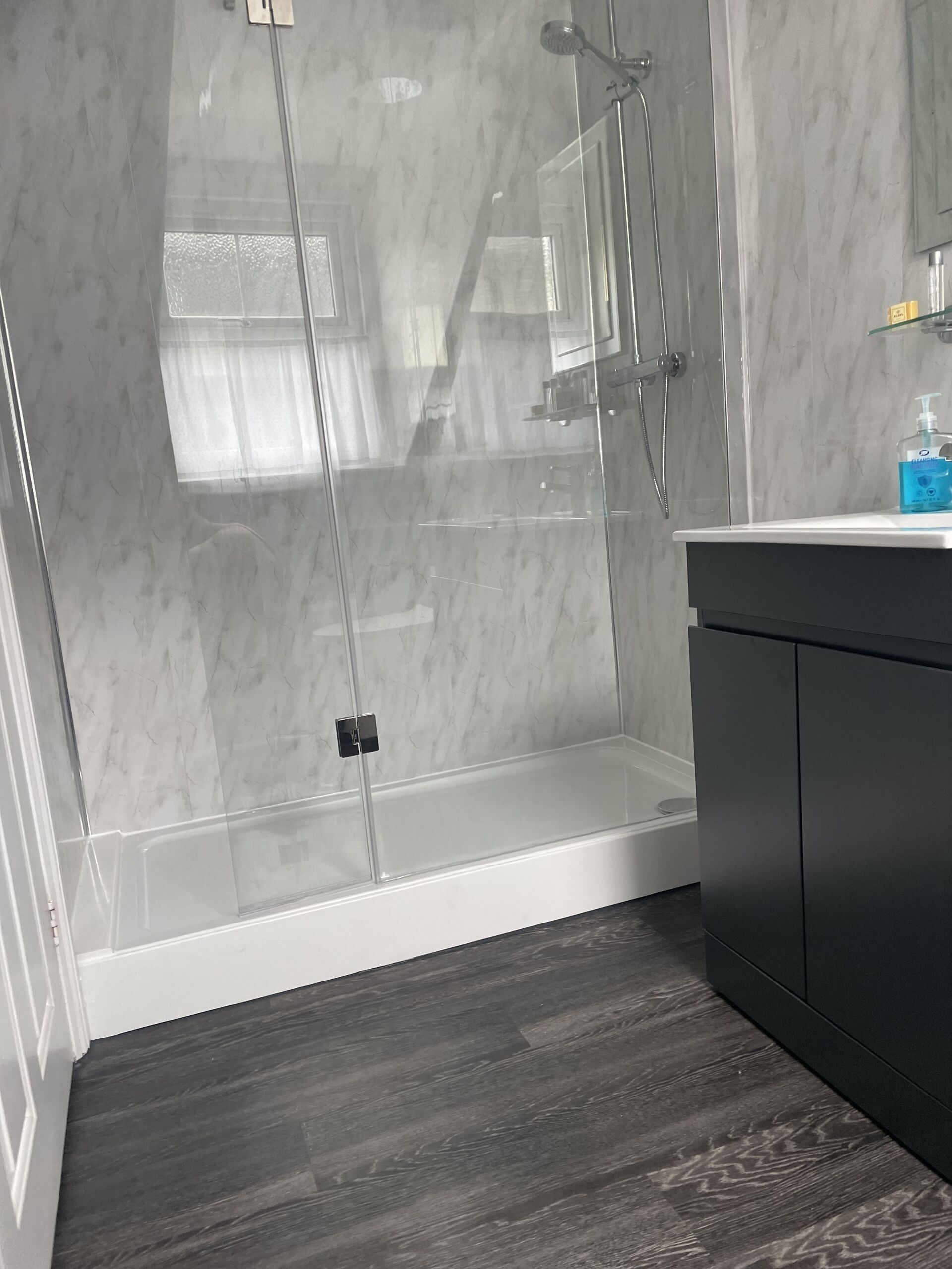 A modern bathroom with a glass shower enclosure, a dark wood floor, and a white vanity with a dark cabinet.