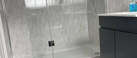 A modern bathroom with a glass shower enclosure, a dark wood floor, and a white vanity with a dark cabinet.