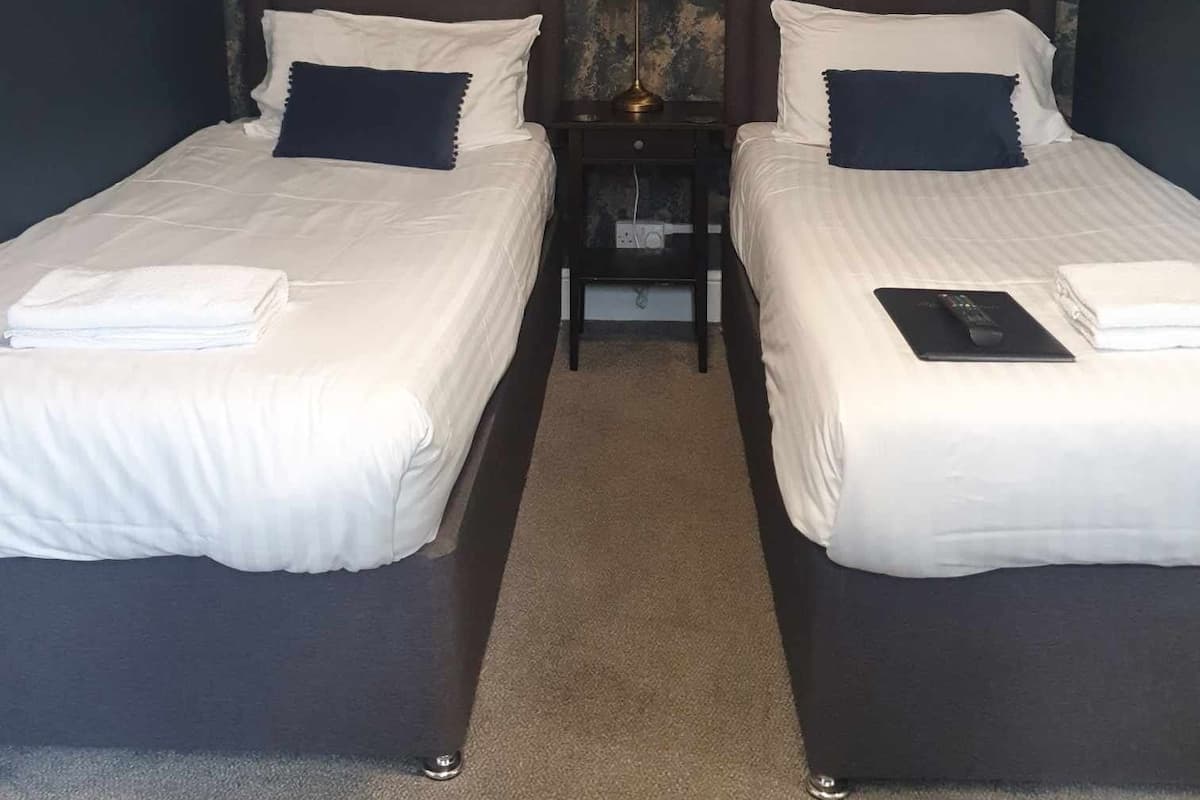 Quarto de hotel com duas camas, mesa de cabeceira com abajur e parede texturizada.