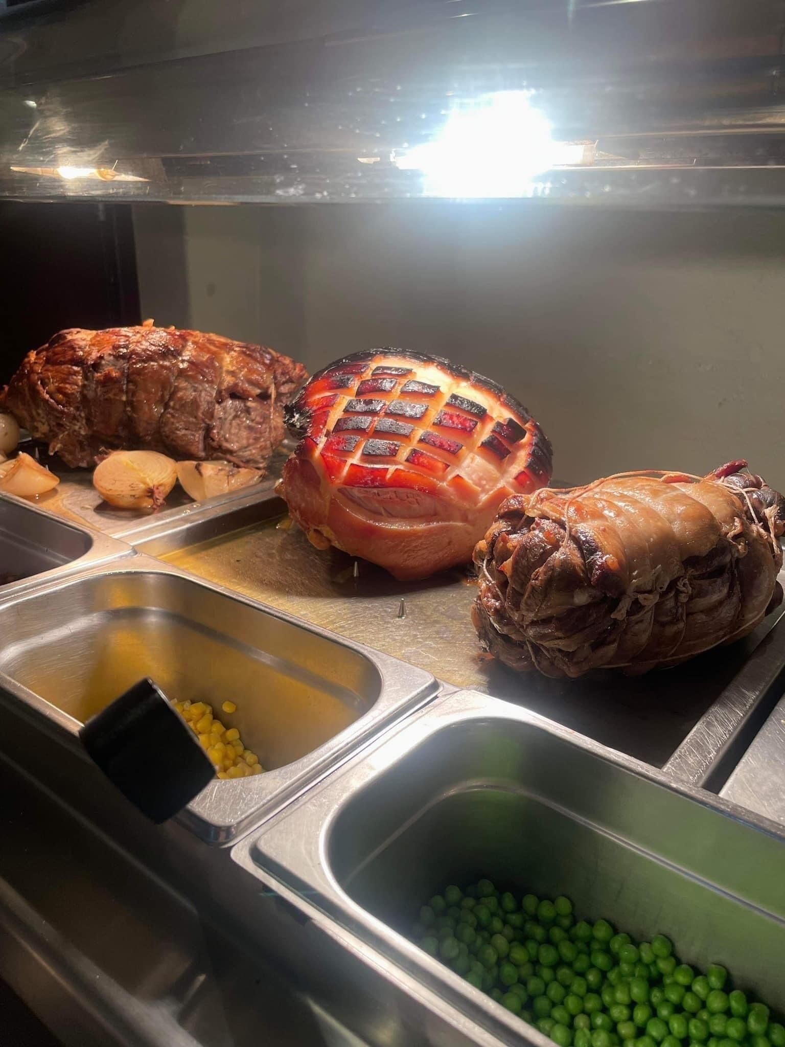 Un bufé con carnes asadas, patatas y guisantes verdes.