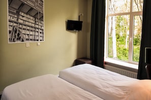 Habitación de hotel con cama, estantería, televisor y ventana con vistas a árboles.