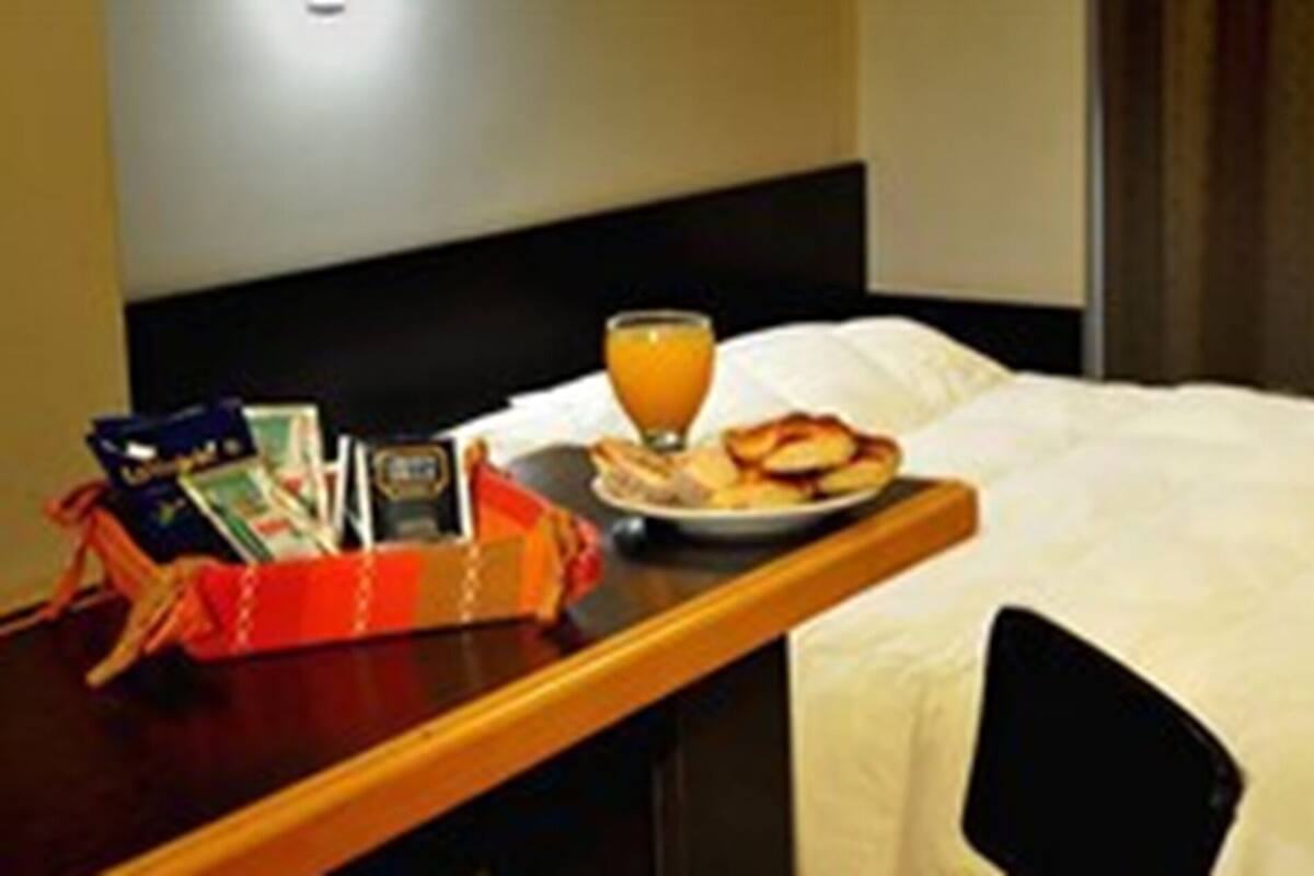 Une chambre d’hôtel avec un lit, une table de chevet sur laquelle se trouve un verre de jus d’orange, une assiette de nourriture et un téléviseur fixé au mur.