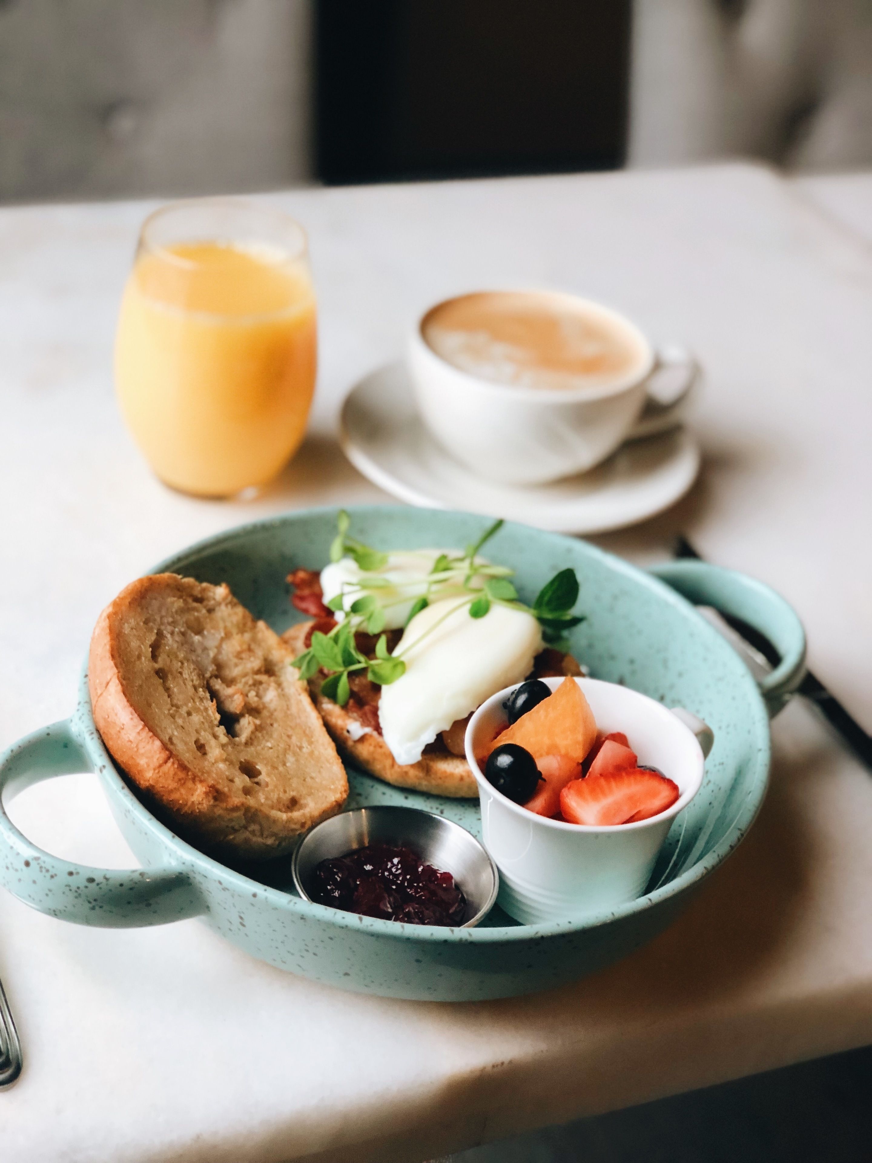 A breakfast plate with toast, eggs, and berries, a cup of coffee, and a glass of orange juice on a table.