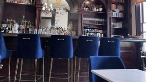 Un espace bar agrémenté d’un lustre, de tabourets de bar bleus et d’étagères remplies de bouteilles.