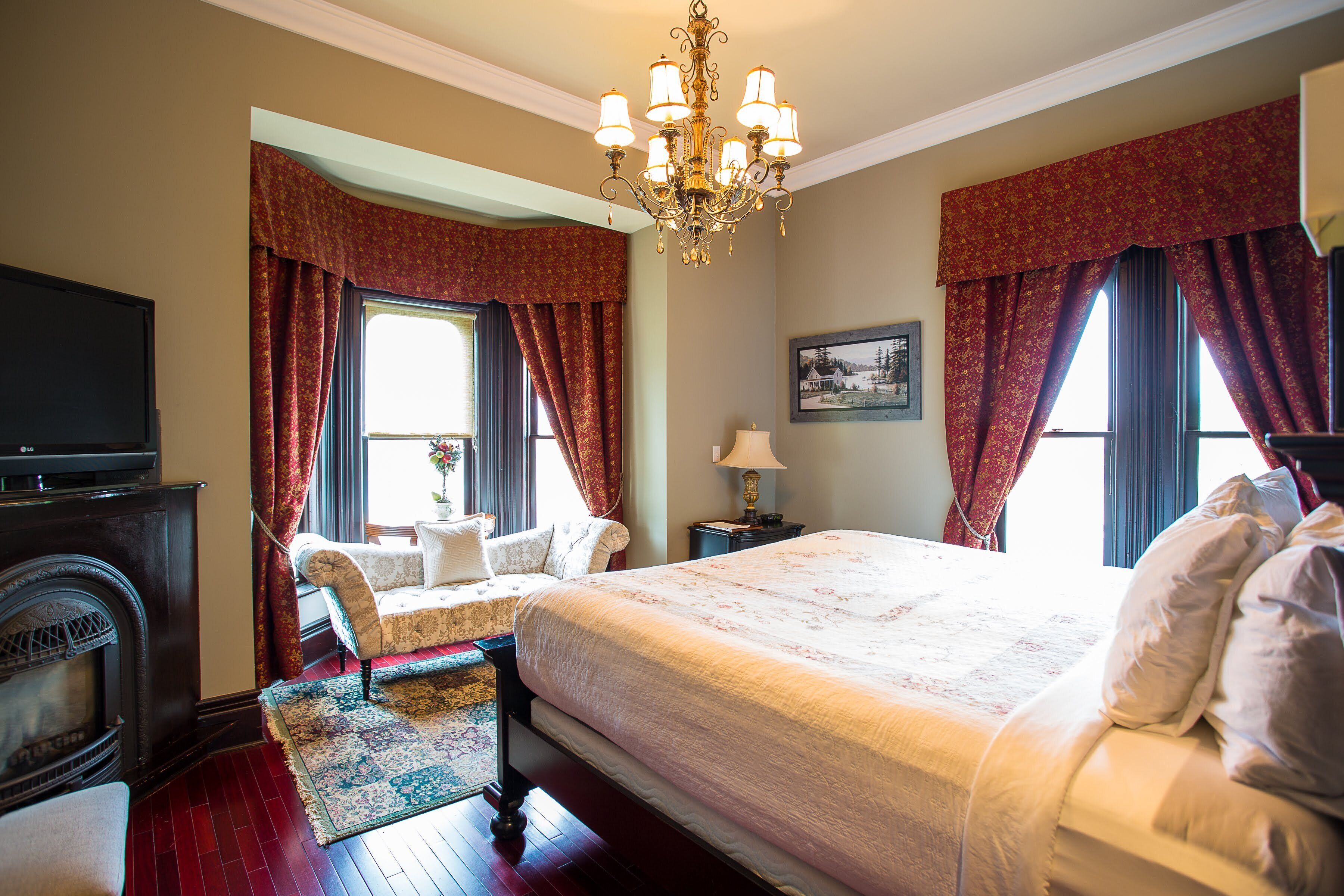 Een hotelkamer met een groot bed, een zithoek met een stoel, een open haard en een kroonluchter.