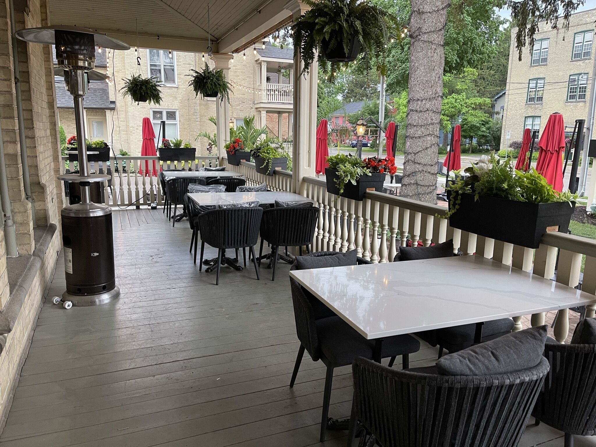 An outdoor patio with tables and chairs, surrounded by a white picket fence, and potted plants.