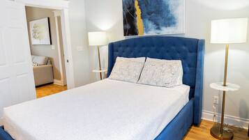 Een slaapkamer met een groot bed, twee bedlampen, een blauw hoofdeinde en een schilderij aan de muur.