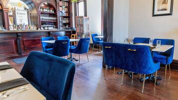 Un restaurante con sillas de terciopelo azul, una zona de bar con estantería, y un cartel que dice "Ridicom House 1868".