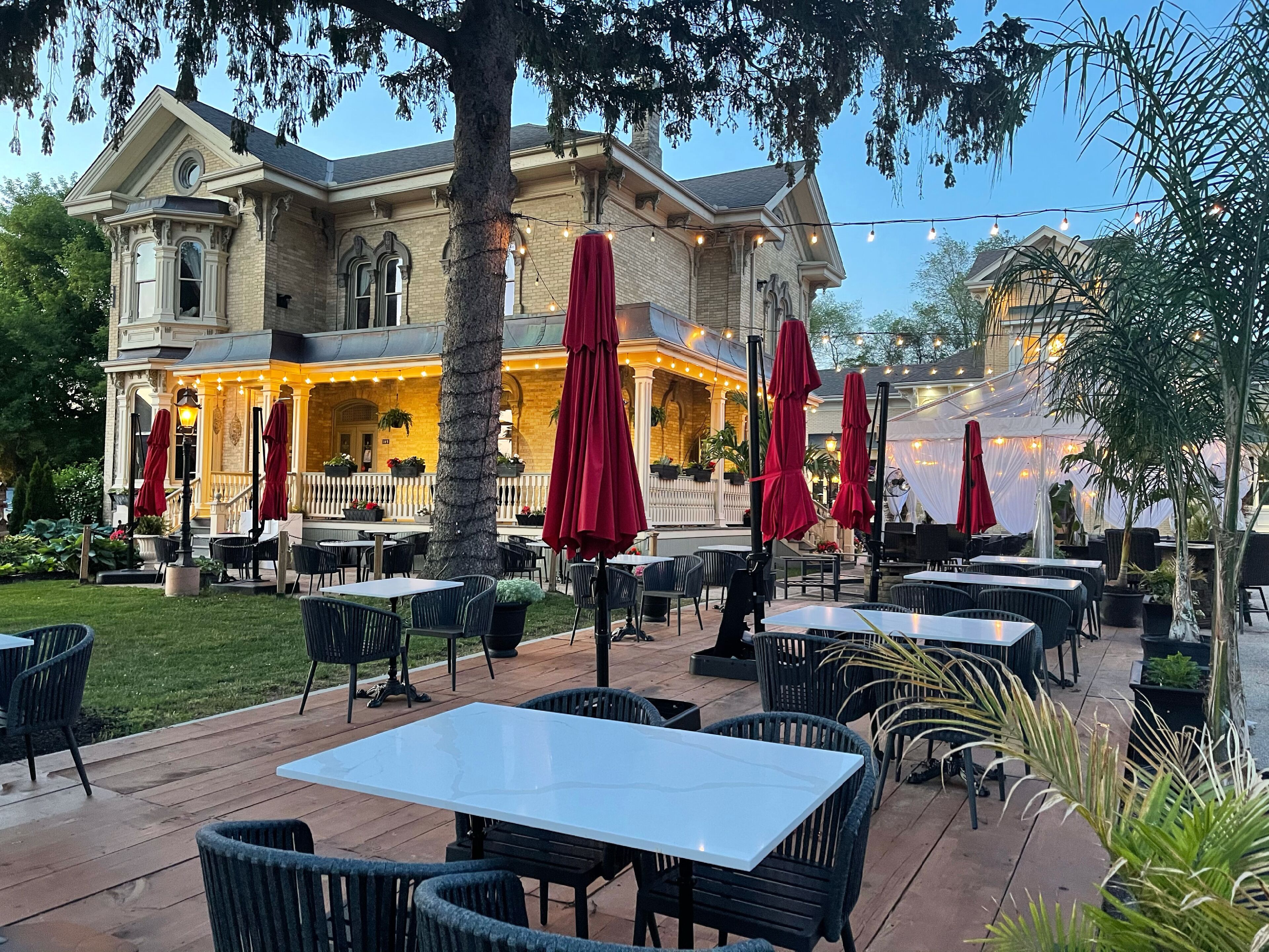 An outdoor patio with tables and chairs, surrounded by a brick building with a balcony.