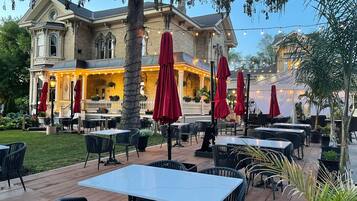 An outdoor patio with tables and chairs, surrounded by a brick building with a balcony.