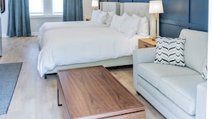 Une chambre d’hôtel moderne avec un grand lit, un canapé, une table basse en bois et un mur décoré de tableaux encadrés.