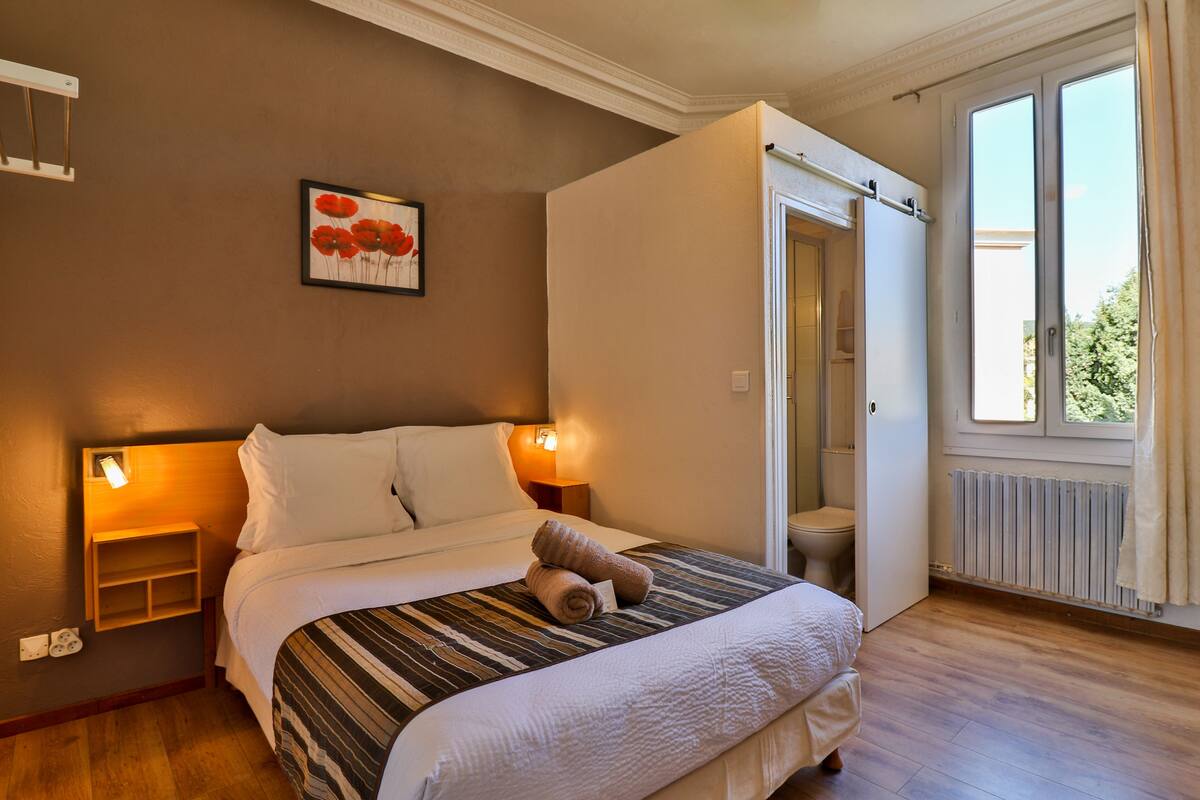 A neatly arranged bedroom with a bed, bedside lamps, a framed artwork, and a window with curtains.