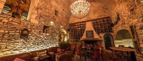 A cozy interior with stone walls, a chandelier, leather seating, and a wine rack.
